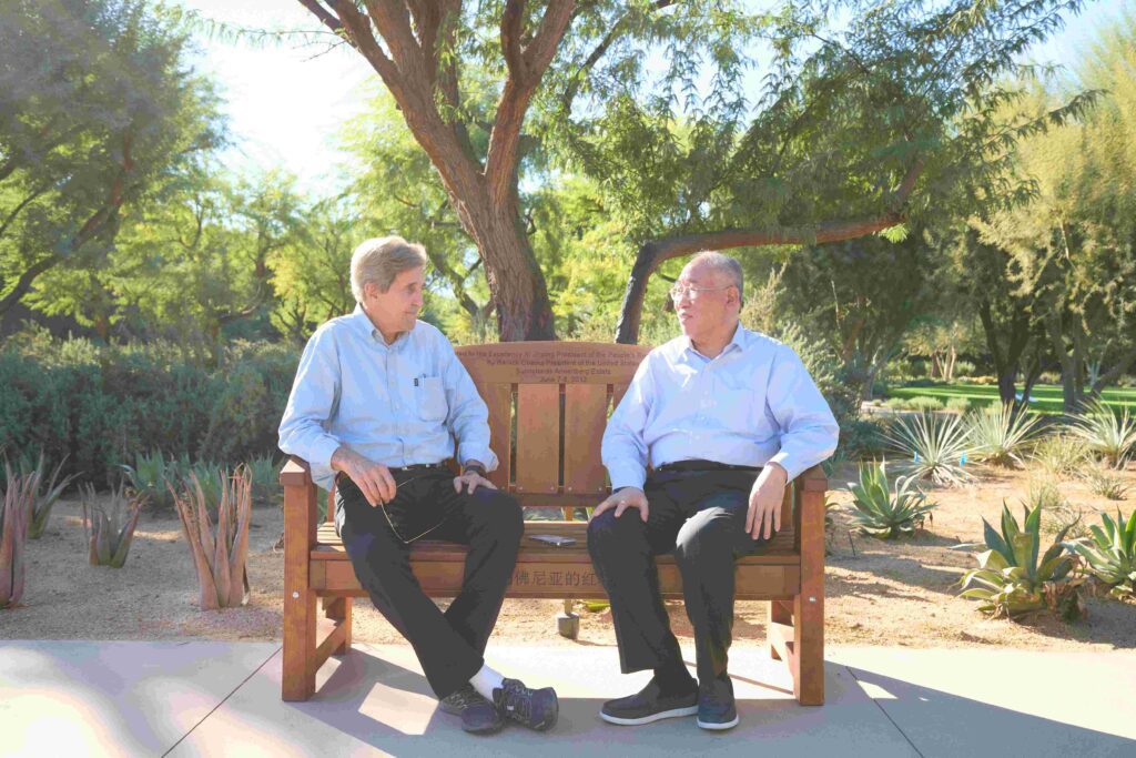 Former Secretary of State John Kerry, the U.S. Special Presidential Envoy for Climate, and his counterpart from China, Minister Xie Zhenhua, sit on a replica of the bench that the United States gifted to China in a 2013 summit at Sunnylands.